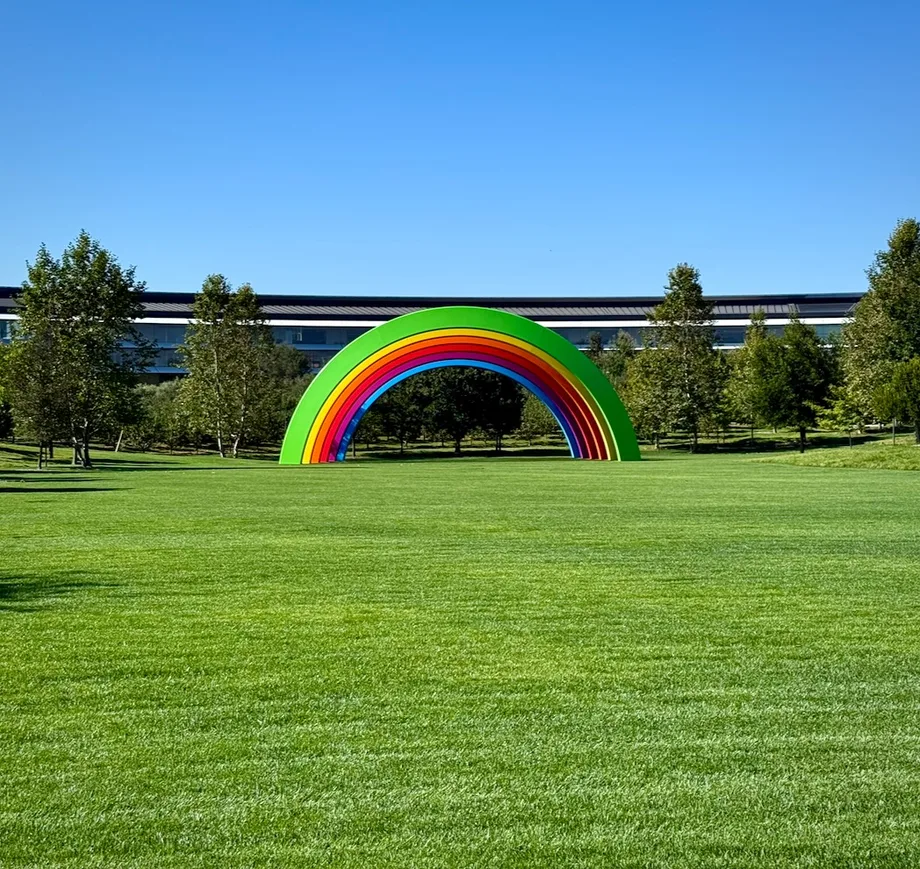 The rainbow arch sculpture on the lawn at Apple Park, with the main building behind it.